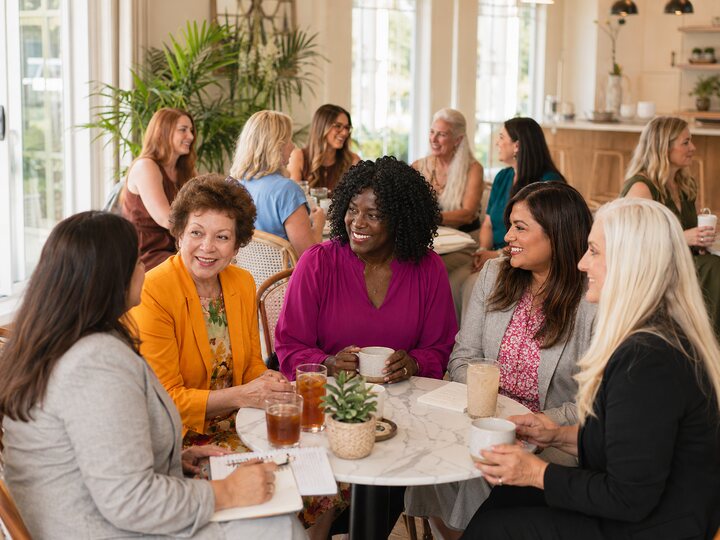 A diverse group of women networking in a relaxed bright professional setting.